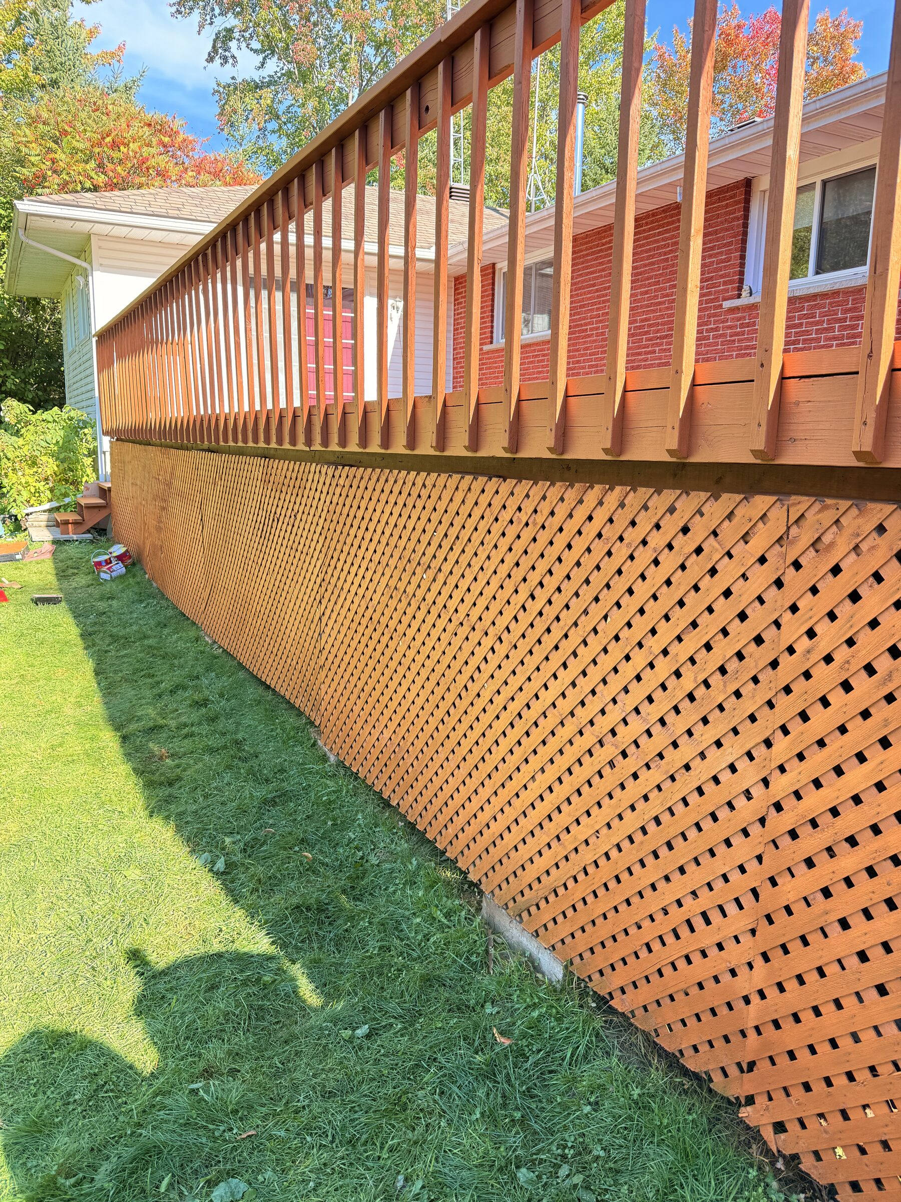 Freshly stained deck with matching railing and diamond lattice skirting against a red brick wall
