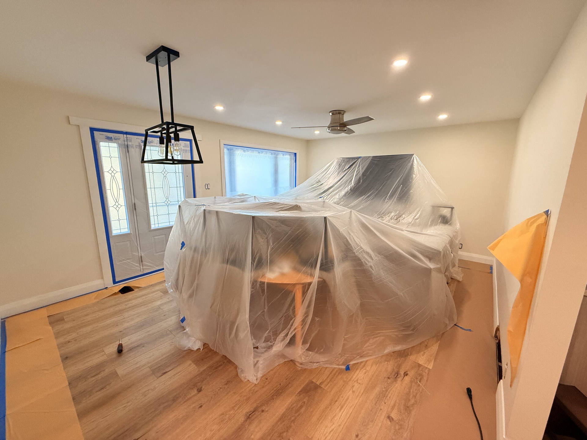 Living room prepped for interior painting, furniture wrapped in plastic and floors covered